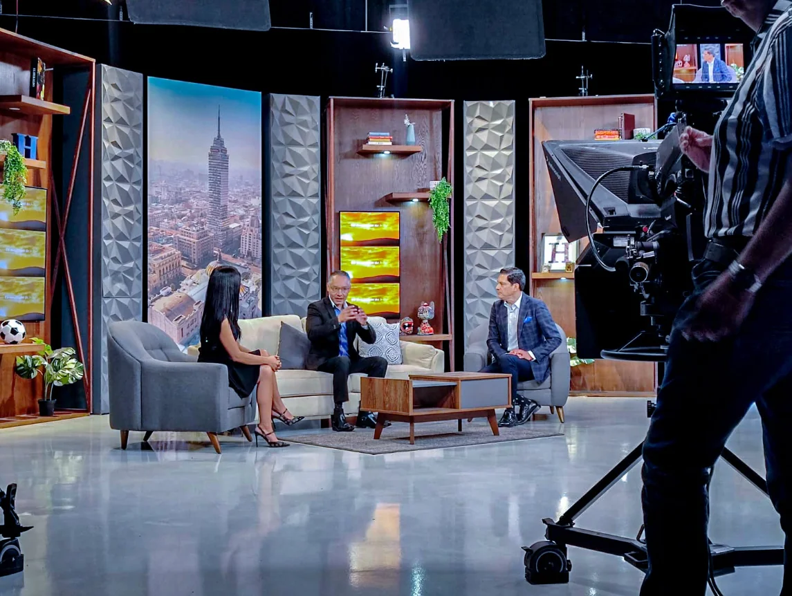 Set de televisión con entrevista en vivo y equipo de producción alrededor.